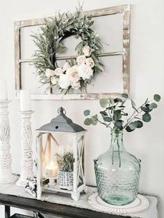 a table topped with vases filled with flowers next to a wall mounted sign and candle