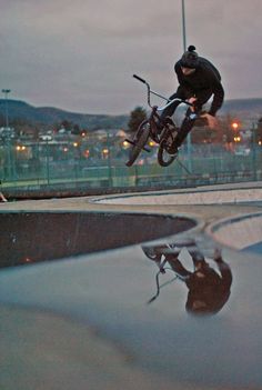 a man flying through the air on top of a bike next to a puddle in a parking lot