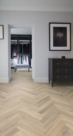 an empty room with wooden floors and clothes on hangers in the closet, next to a chest of drawers