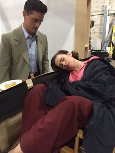 a man standing next to a woman laying on top of a chair