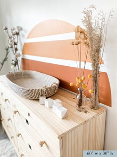 a wooden dresser topped with vases filled with dried flowers next to a wall mounted art piece