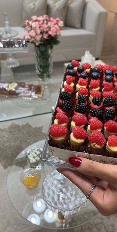 a person holding up a cake with fruit on it in front of a glass table