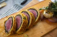 a wooden cutting board topped with sliced meat and veggies on top of it