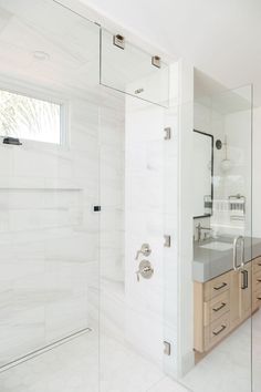 a bathroom with a glass shower door and white tile flooring, along with wooden cabinetry