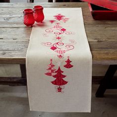 the table is set with two red glasses and a christmas tree runner on top of it