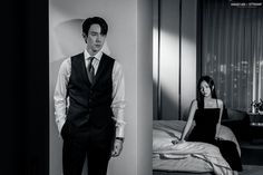 a man in a suit standing next to a woman sitting on a bed