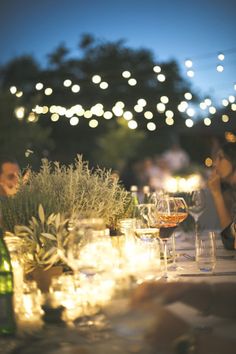 people are sitting at a table with wine glasses and candles in front of the tables