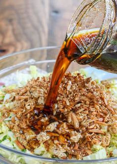 someone pouring dressing into a salad with nuts and lettuce on the side in a glass bowl