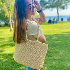 a woman holding a straw bag in her hand and looking into the distance while standing on grass