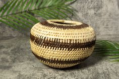 a woven vase sitting on top of a table next to a palm leaf and stone wall