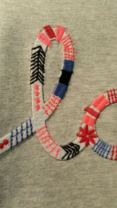 an embroidered t - shirt with the letter q on it and arrows in red, white, and blue