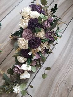 a bridal bouquet with purple and white flowers on a wooden floor next to greenery