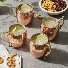 three copper mugs filled with ice and lime next to pretzels