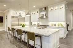 a large kitchen with white cabinets and marble counter tops, along with bar stools