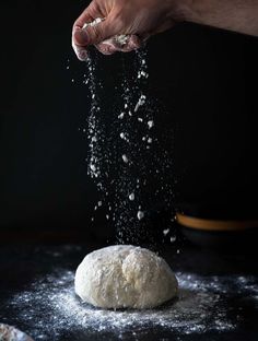 a person sprinkling flour on top of a doughnut