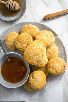 biscuits and honey are on a plate with a spoon next to the bowl full of honey