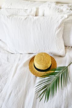 a straw hat and palm leaf on a white bed