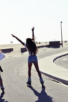 two girls skateboarding down the road with their arms in the air and one girl is holding her hands up