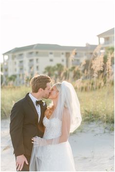 a bride and groom kissing on the beach in front of an oceanfront hotel building