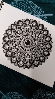 a notebook with an intricate black and white design on the cover, next to a pen