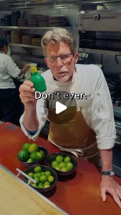 an old man holding a green bottle in front of some bowls of limes on a counter