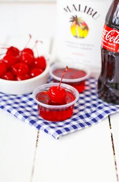 two bowls of cherries next to a bottle of coca - cola on a blue and white checkered tablecloth