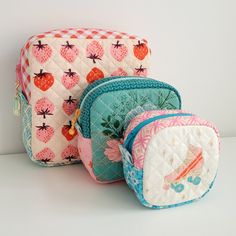 three cosmetic bags sitting next to each other on a white counter top and one has a strawberry design on it