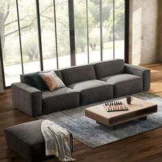 a living room with a couch, coffee table and chess board on the floor in front of large windows