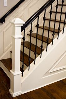 a white stair case with black railing and handrail on wooden flooring in a home