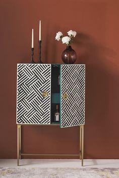 a black and white cabinet with two candles on it next to a vase filled with flowers