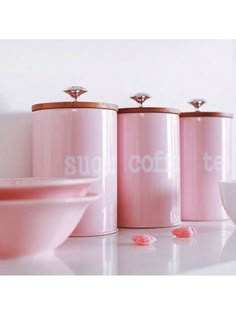 three pink canisters sitting on top of a counter next to a white bowl