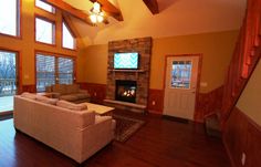 a living room with wood floors and large windows on each side of the wall, along with a stone fireplace