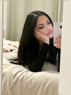 a woman laying on top of a bed holding a cell phone to her face and looking at the camera