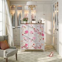 a white closet with pink flowers painted on the doors and drawers next to a chair