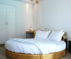 a large bed with white sheets and pillows in a room that has wood flooring