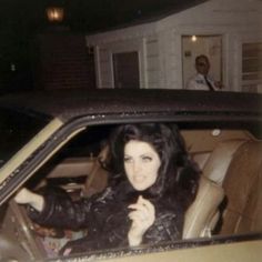 a woman sitting in the driver's seat of a car with her hand up