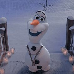 there is a snowman that has been decorated with candles and lights in front of him