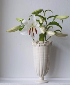 a white vase with flowers in it sitting on a shelf