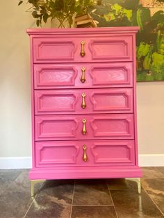 a pink dresser with gold handles and knobs on the drawers is next to a potted plant