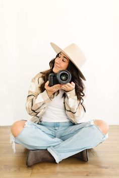 a woman sitting on the floor with a camera in her hand and wearing a cowboy hat