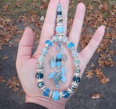 a hand is holding a necklace with blue beads and leaves on it's side