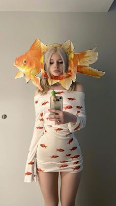 a woman with fish on her head holding a cell phone and taking a selfie