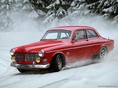 an old red car driving through the snow