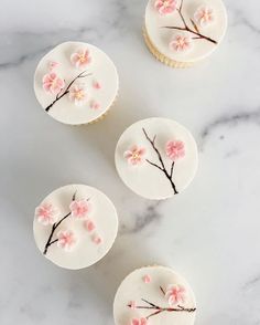 four cupcakes decorated with white frosting and pink flowers on top of a marble table