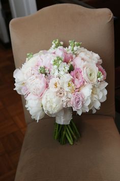 a bouquet of white and pink flowers sitting on top of a brown chair in front of a wooden floor