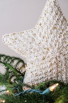 a white knitted star ornament on top of a christmas tree with lights