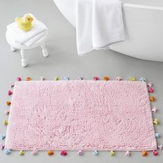 a pink rug with pom poms on it next to a white bath tub