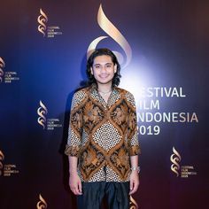 a man standing in front of a blue and purple wall with the words festival film indonesia on it