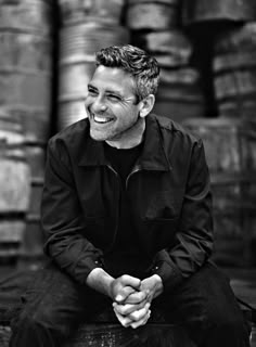 a man sitting on top of a wooden bench next to stacks of beer barrels in black and white