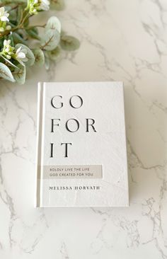 a book sitting on top of a white table next to some green leaves and flowers